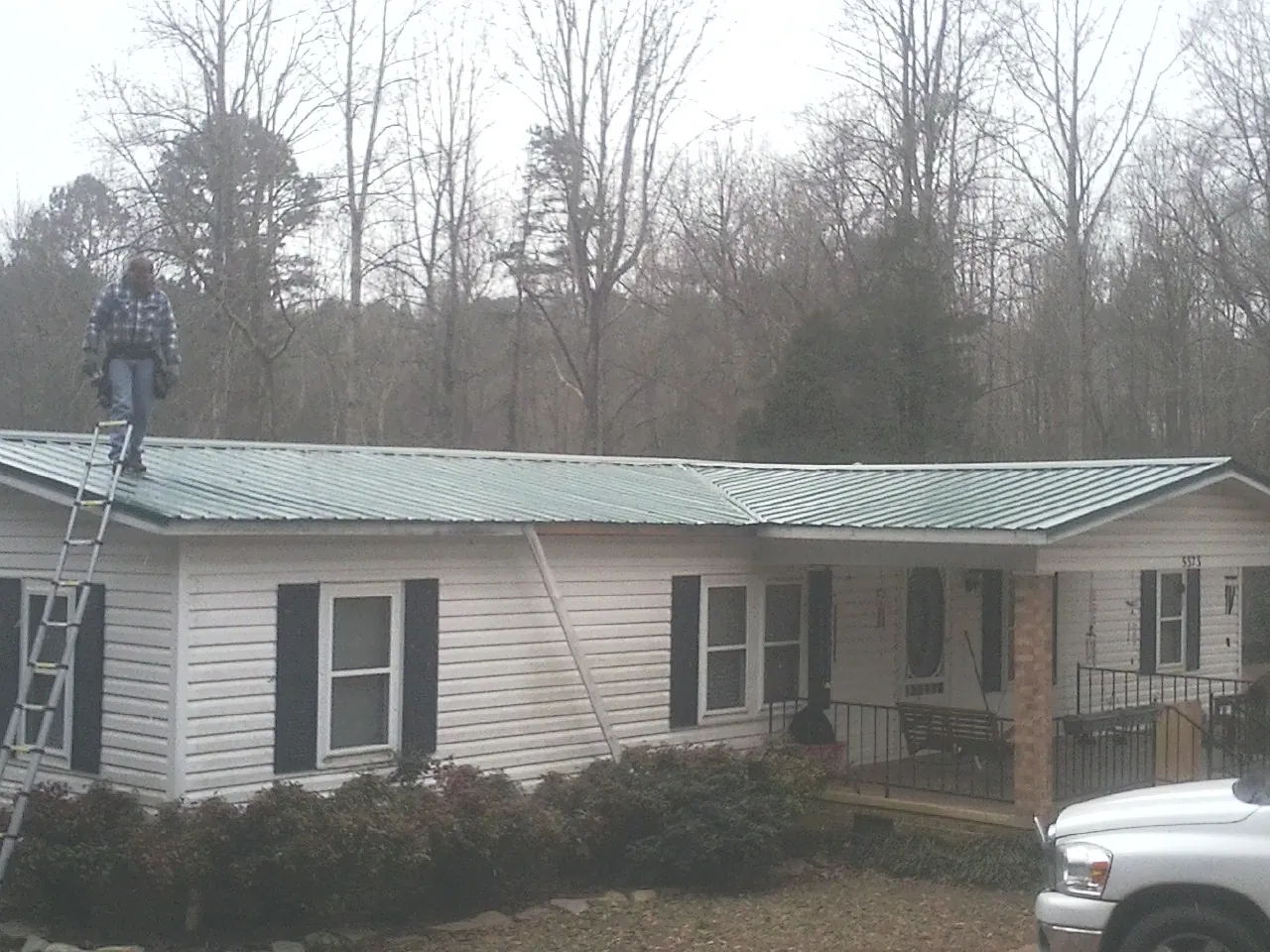 Worker on a ladder beside a new green metal roof on a ranch home in Preston